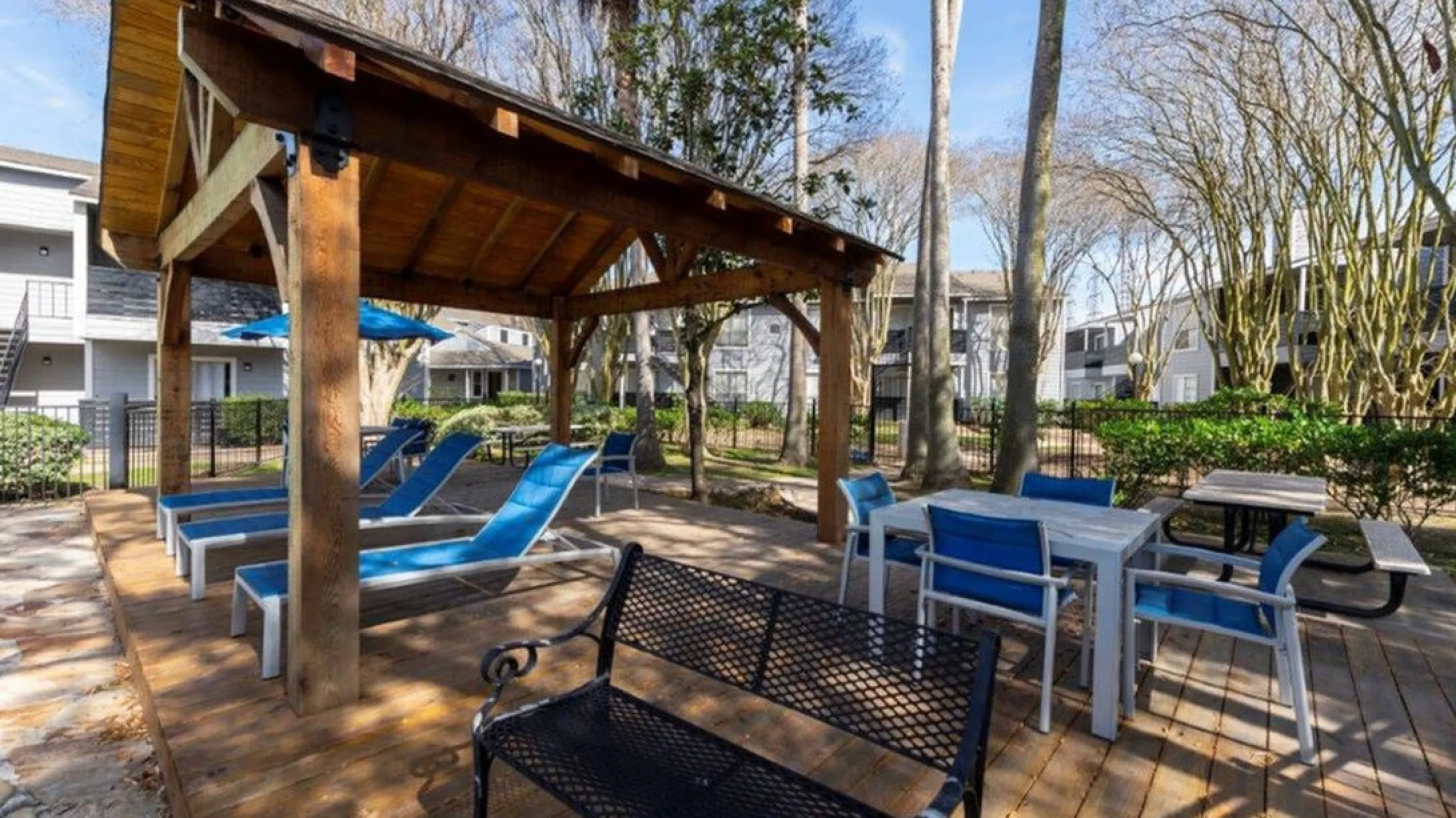 Charming outdoor living space with a covered wooden pergola, comfortable lounge chairs, and modern dining area, surrounded by lush greenery for a serene retreat.