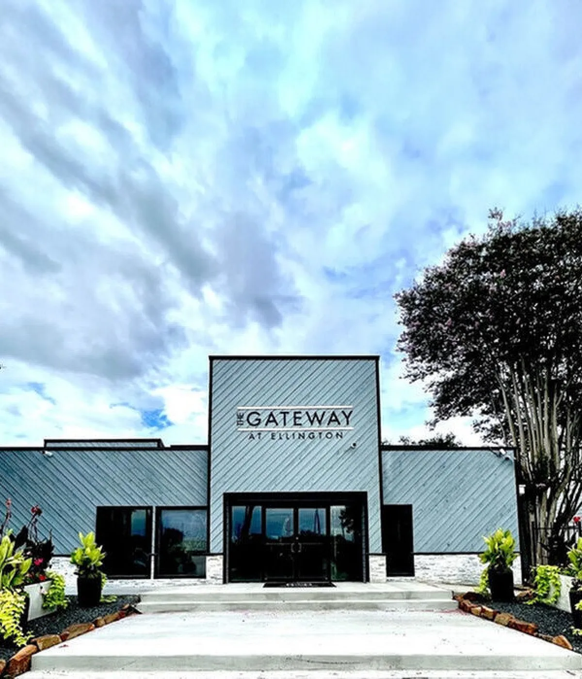 Elegant entrance of The Gateway at Ellington, featuring modern architecture with lush landscaping and a welcoming atmosphere under a vibrant sky.