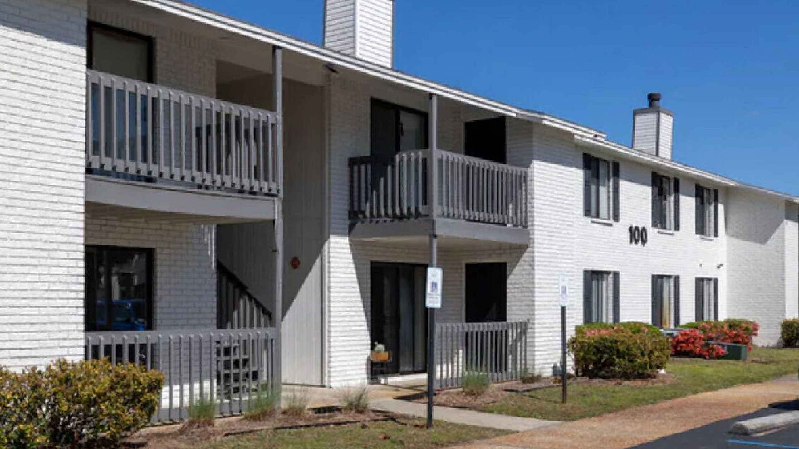 Contemporary white brick apartment building with private balconies and lush landscaping, offering modern living in a serene setting.