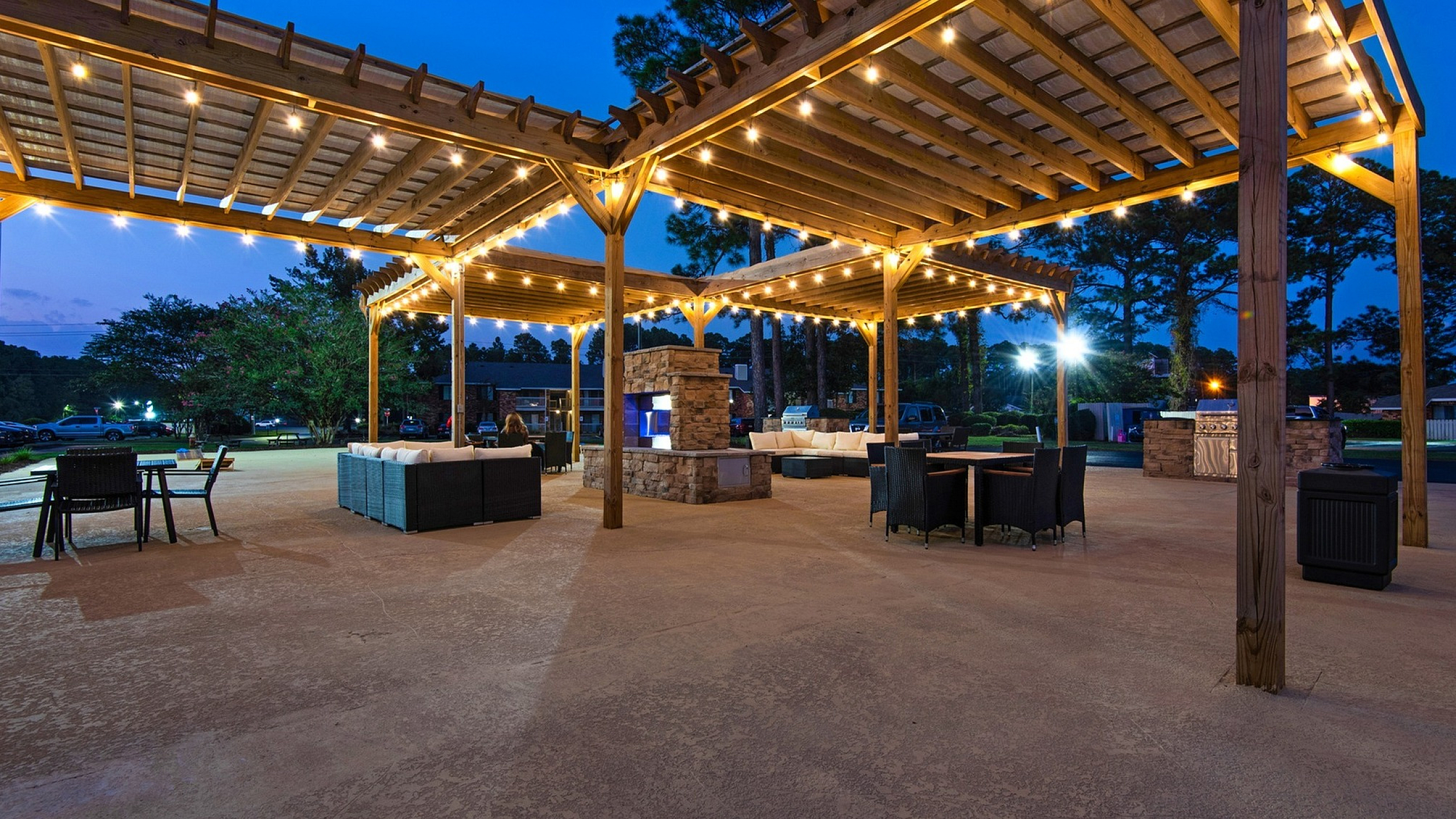 Charming outdoor terrace with elegant pergola and cozy lighting, featuring sophisticated seating areas and a modern stone fireplace.