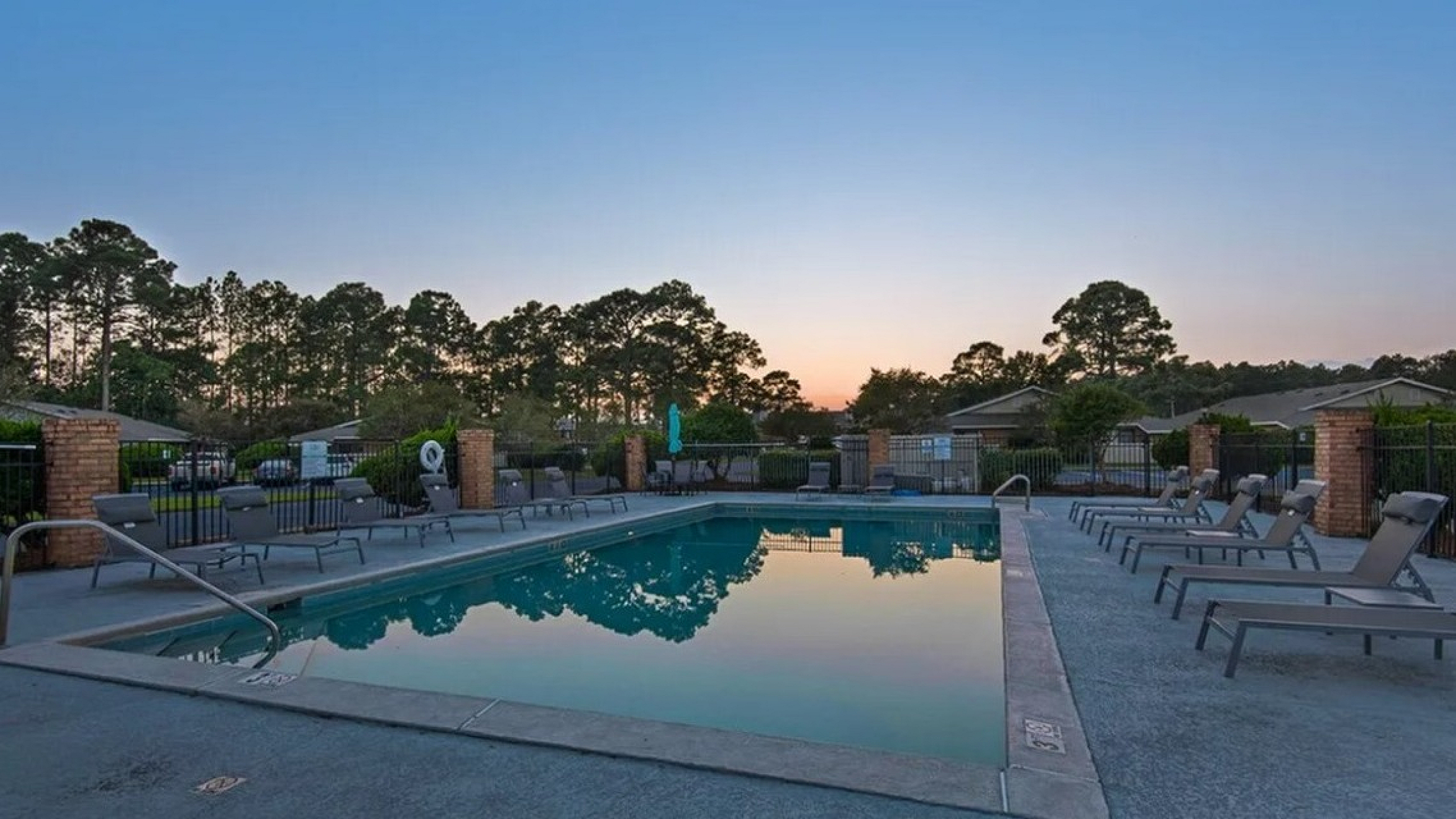 Serene evening view of a swimming pool surrounded by comfortable lounge chairs, capturing a tranquil sunset ambiance.