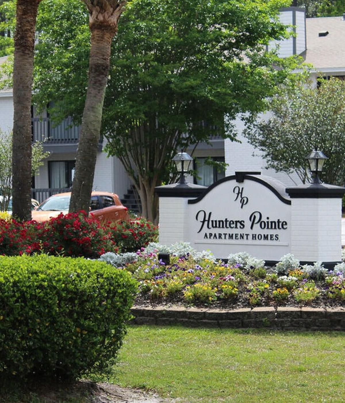 Elegant entrance of Hunters Pointe Apartment Homes with lush landscaping, vibrant flowers, and welcoming signage.