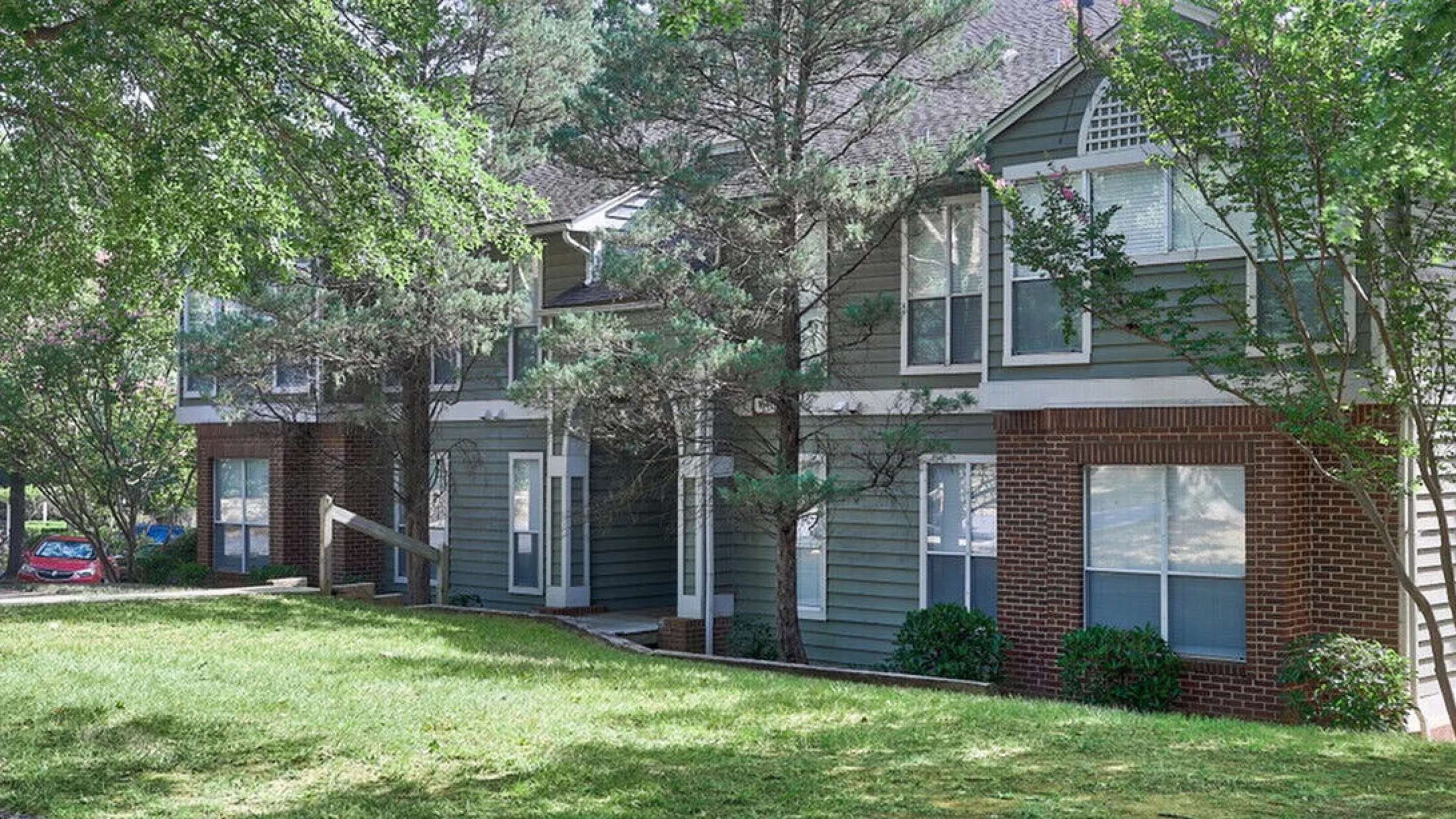 Charming townhouse exterior surrounded by lush greenery and mature trees with spacious windows and inviting entrance.