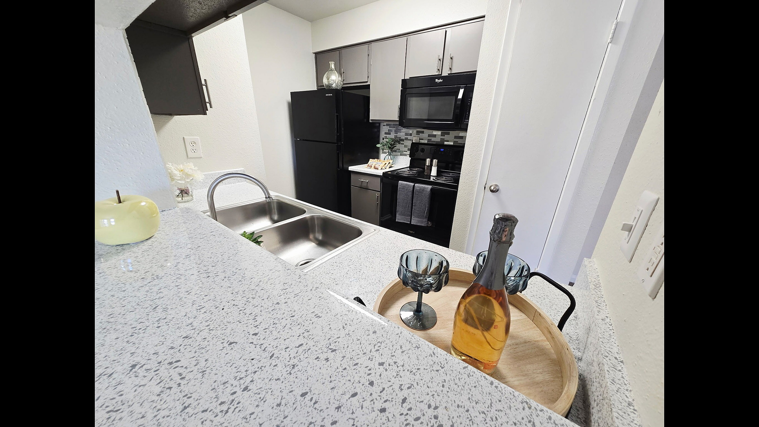 Modern kitchen with elegant countertop, double sink, sleek appliances, and stylish decor featuring a bottle and glasses.
