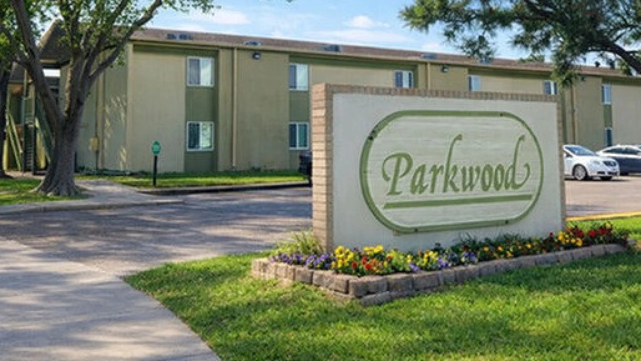 Inviting Parkwood apartment exterior with well-maintained greenery and vibrant flower beds under a clear blue sky.