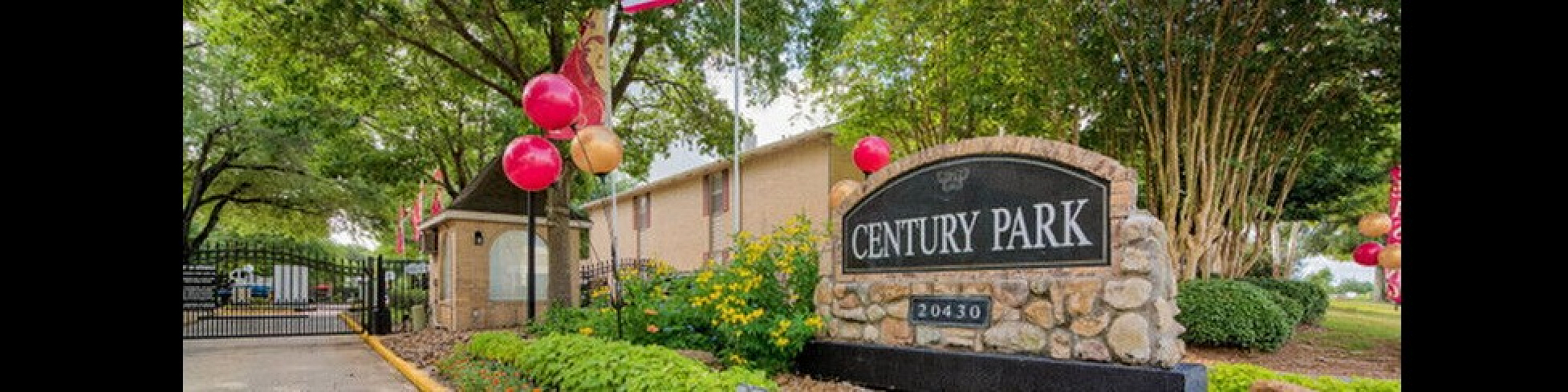 Inviting entrance of Century Park, showcasing vibrant landscaping, colorful balloons, and a welcoming community vibe.