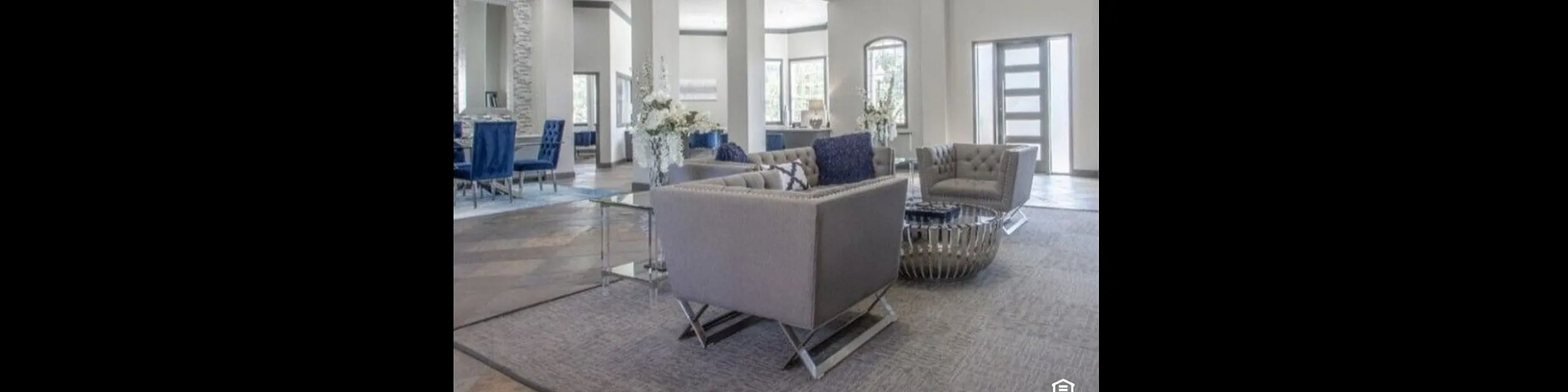 Elegant apartment lobby with modern gray seating, blue accents, and a stunning chandelier under high ceilings.
