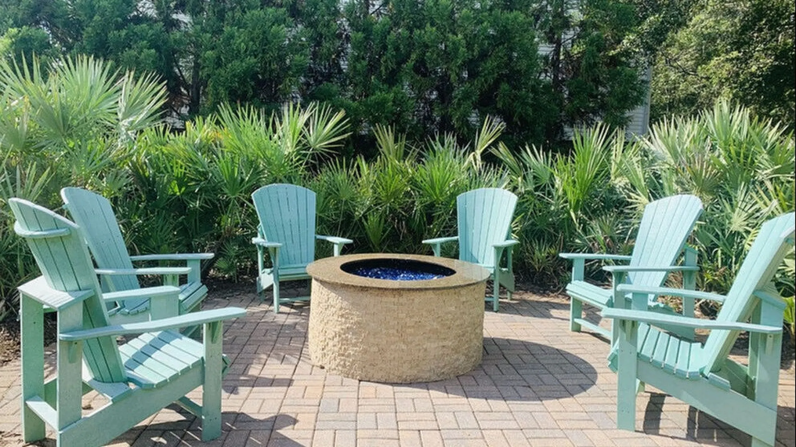 Inviting outdoor seating area with teal Adirondack chairs surrounding a stylish fire pit, set against lush green landscaping.