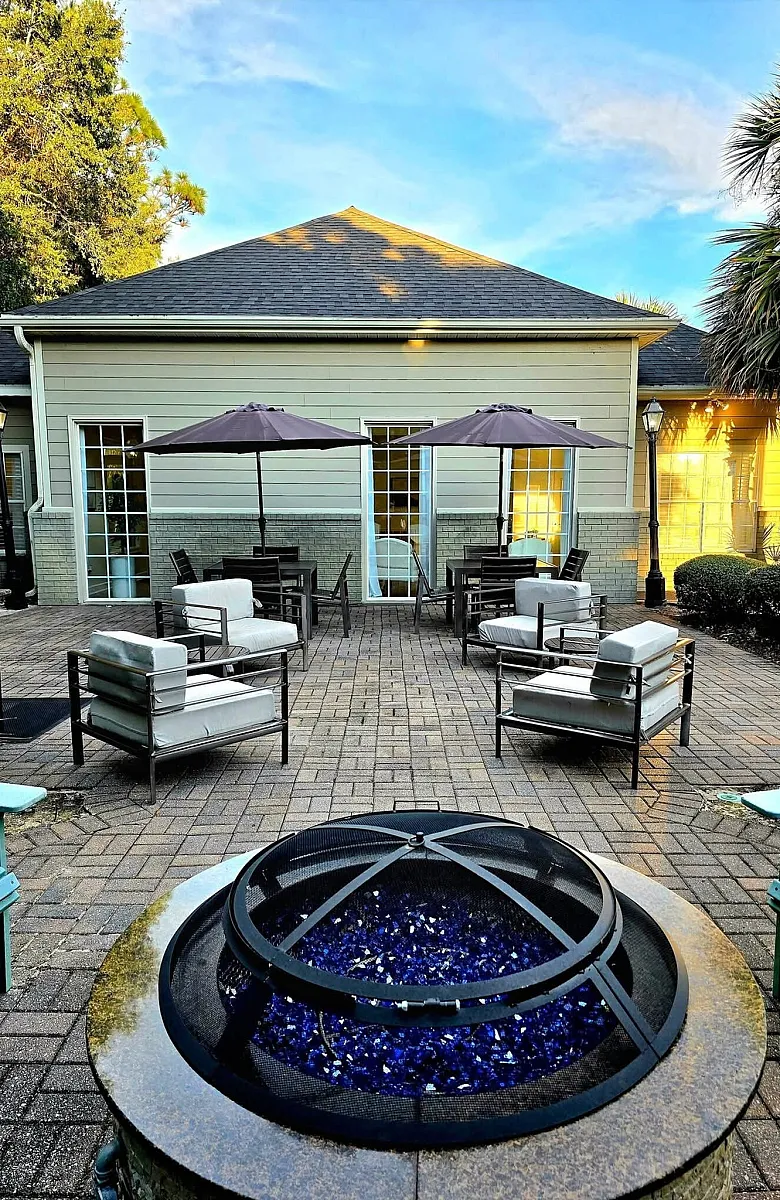 Charming outdoor patio with comfortable seating, shaded by stylish umbrellas, featuring a modern fire pit with vibrant blue glass accents.
