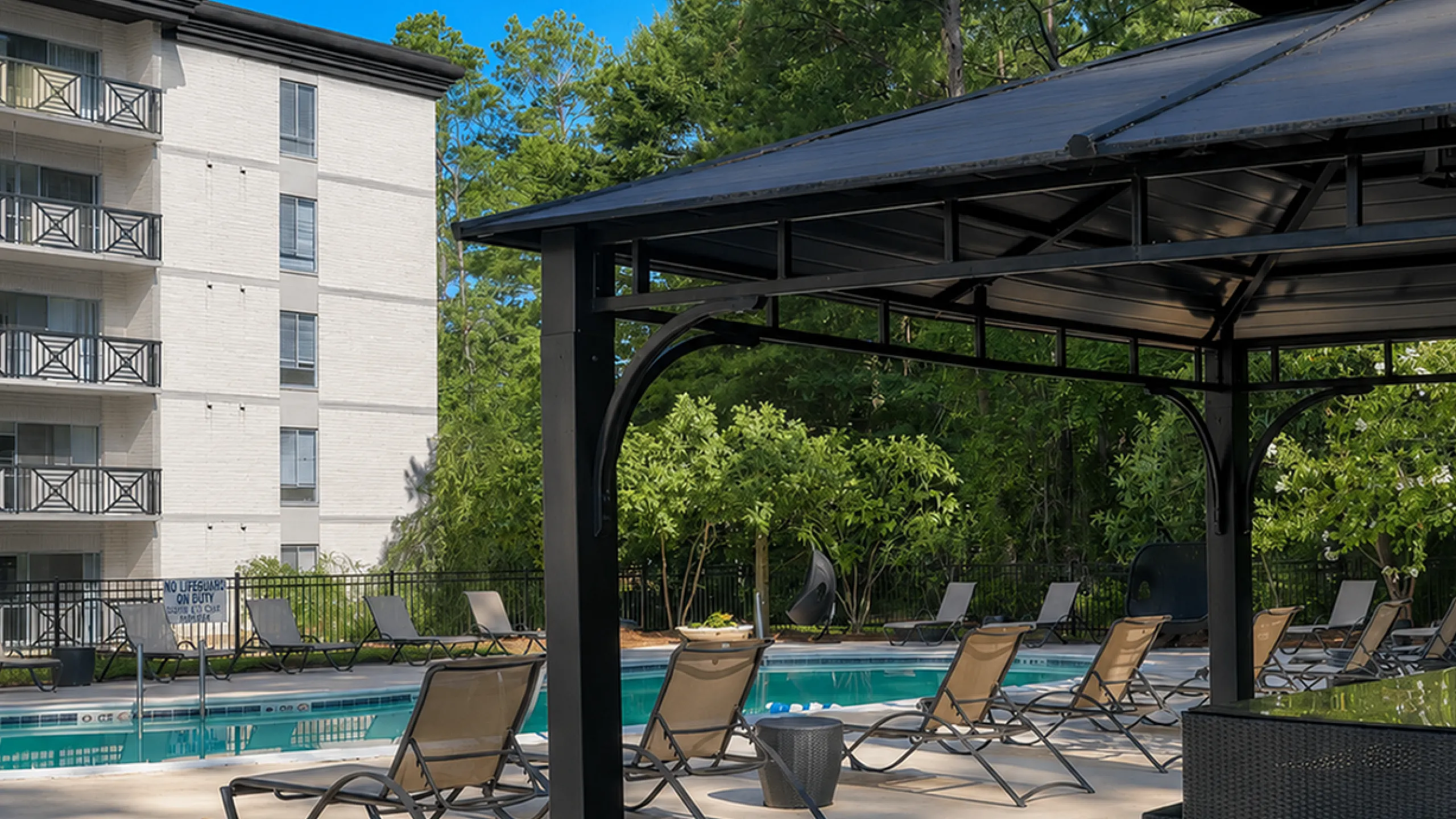 Elegant apartment complex featuring a serene outdoor pool area with stylish lounge chairs under lush greenery and a modern gazebo.