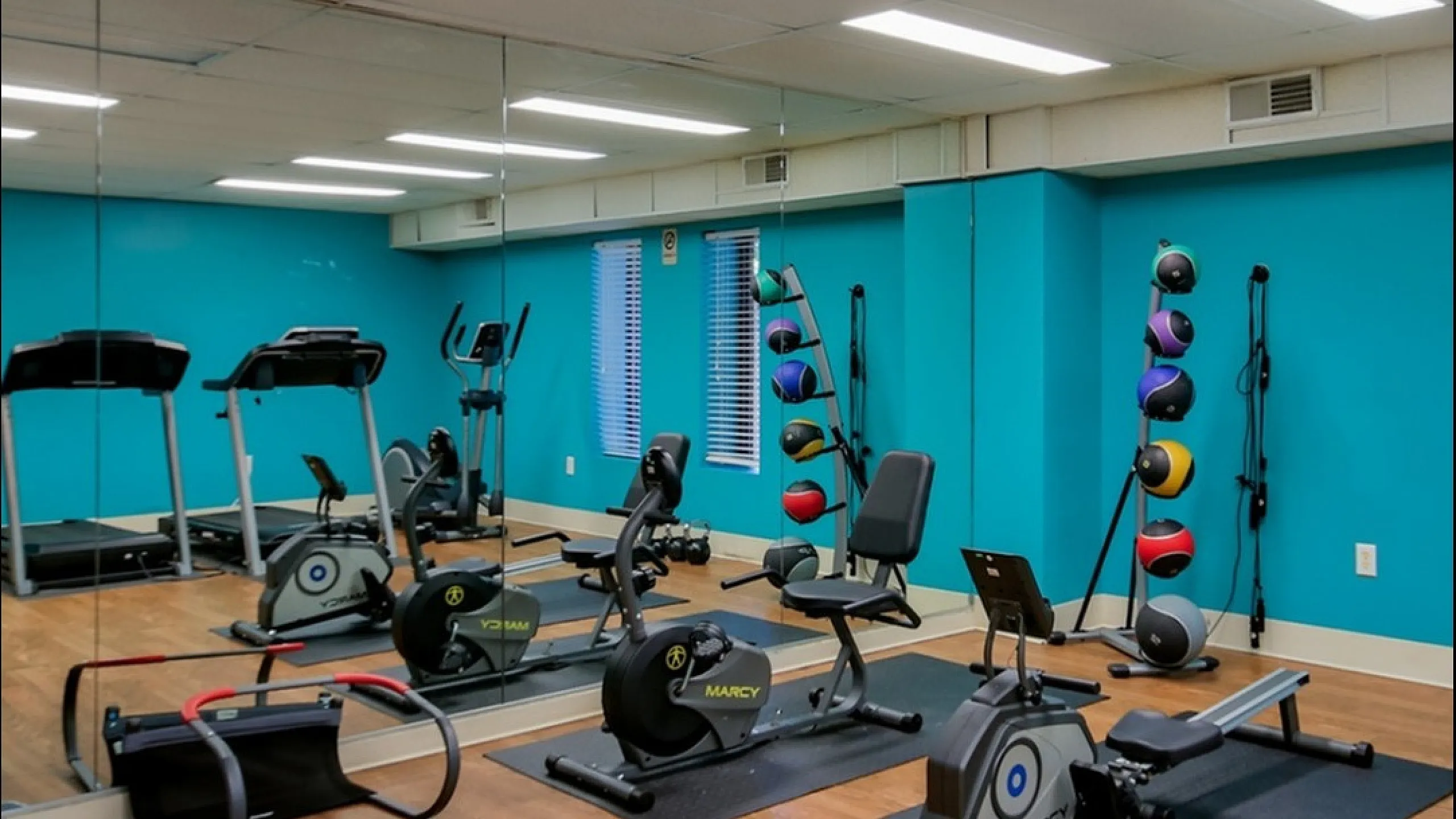 Inviting apartment fitness center with modern exercise equipment and vibrant turquoise walls, ideal for wellness enthusiasts.