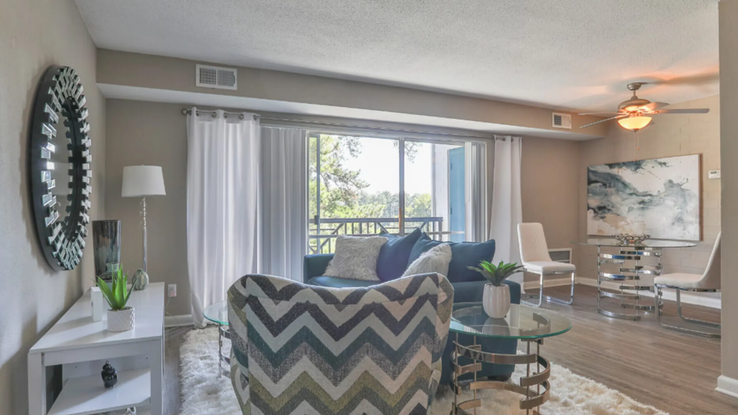 Chic living room with elegant decor, featuring a plush chevron chair, glass coffee tables, and a spacious balcony view.