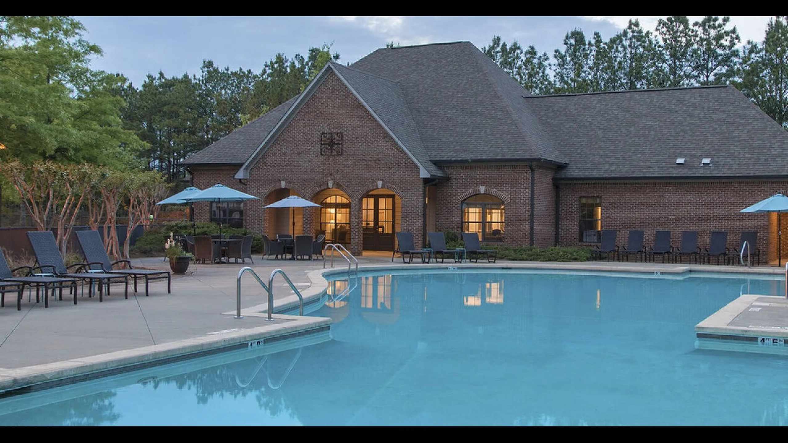 Charming apartment complex featuring a sparkling outdoor pool, elegant brick clubhouse, and lush green surroundings.