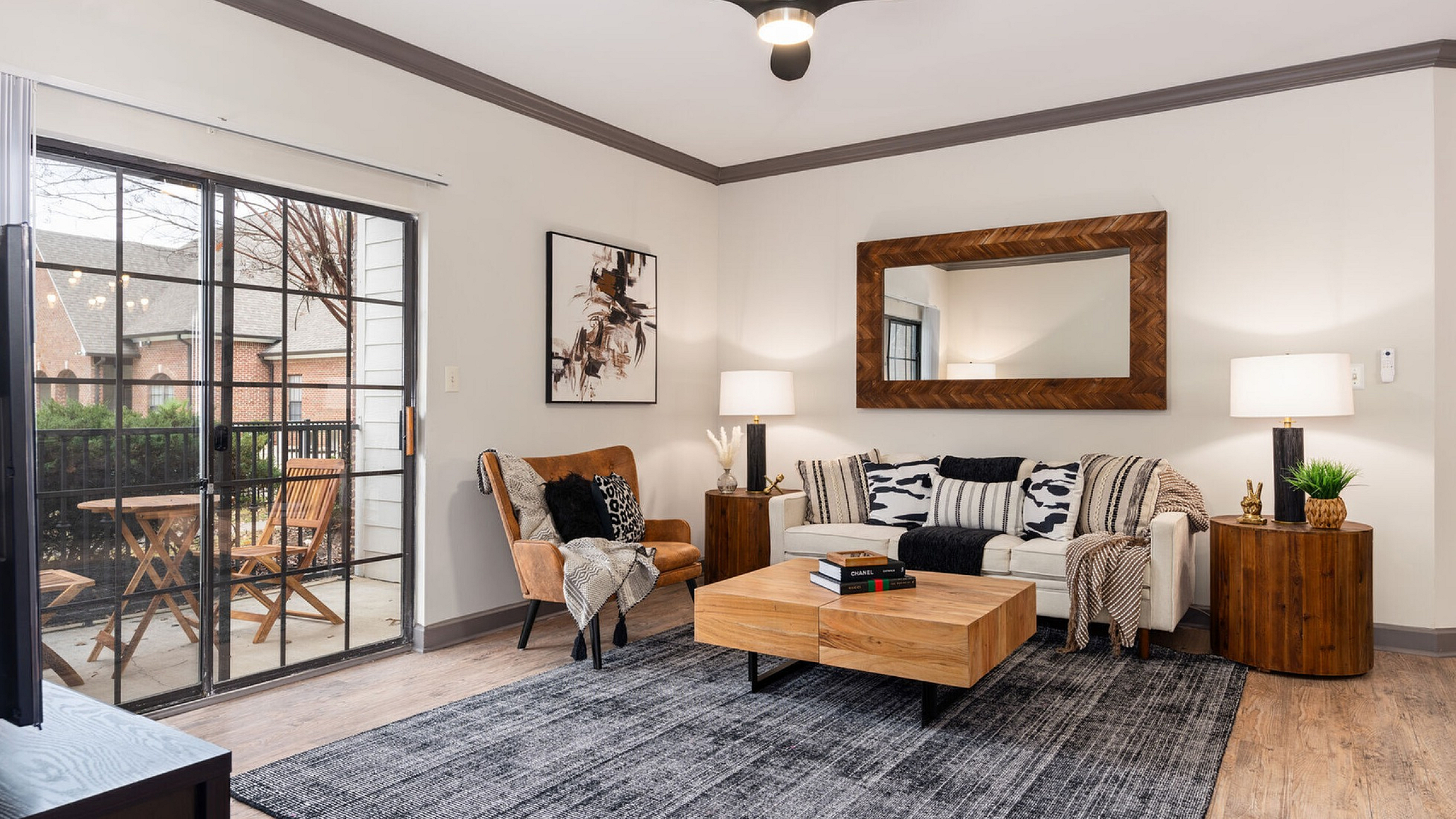 Chic living room with modern decor, a cozy sofa, elegant armchair, and stylish coffee table, illuminated by soft lighting next to a large glass door opening to a charming balcony.