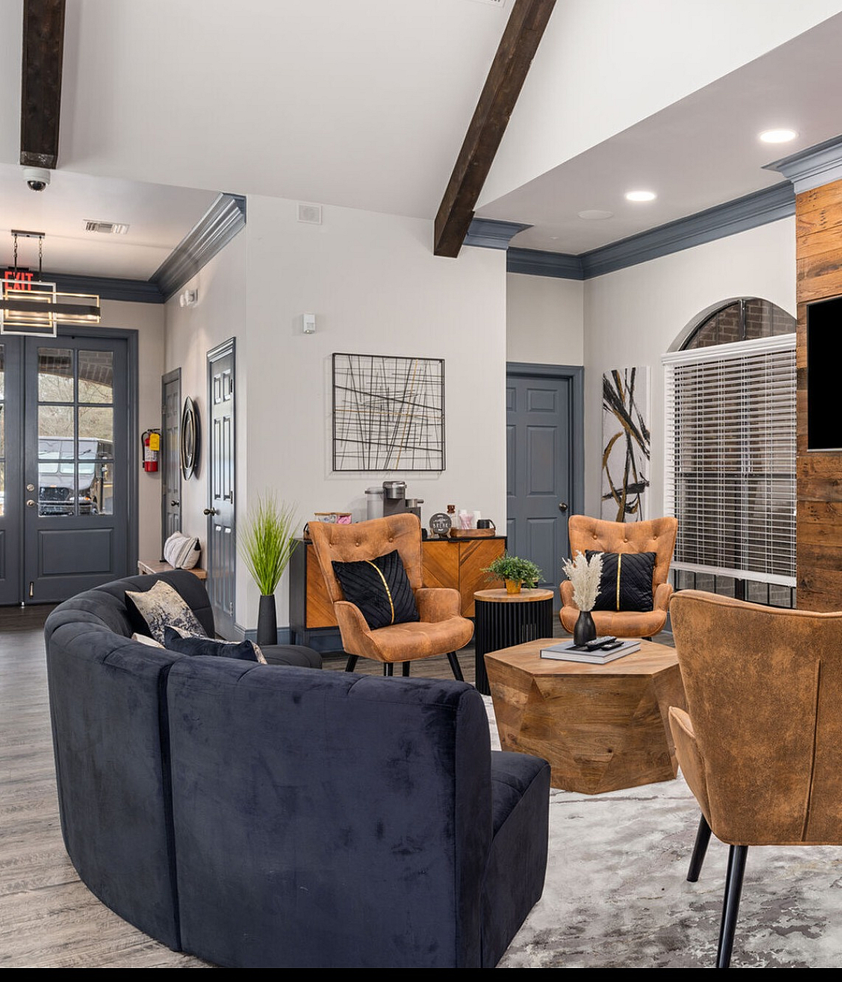 Elegant living room with modern decor, featuring cozy brown armchairs, a plush navy sofa, stylish wooden accents, and a large TV for entertainment.