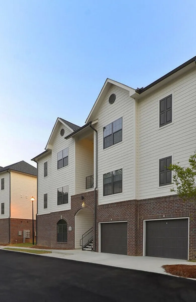 Charming modern apartment complex with elegant brick and siding exterior, featuring spacious garages and lush greenery in a serene neighborhood.