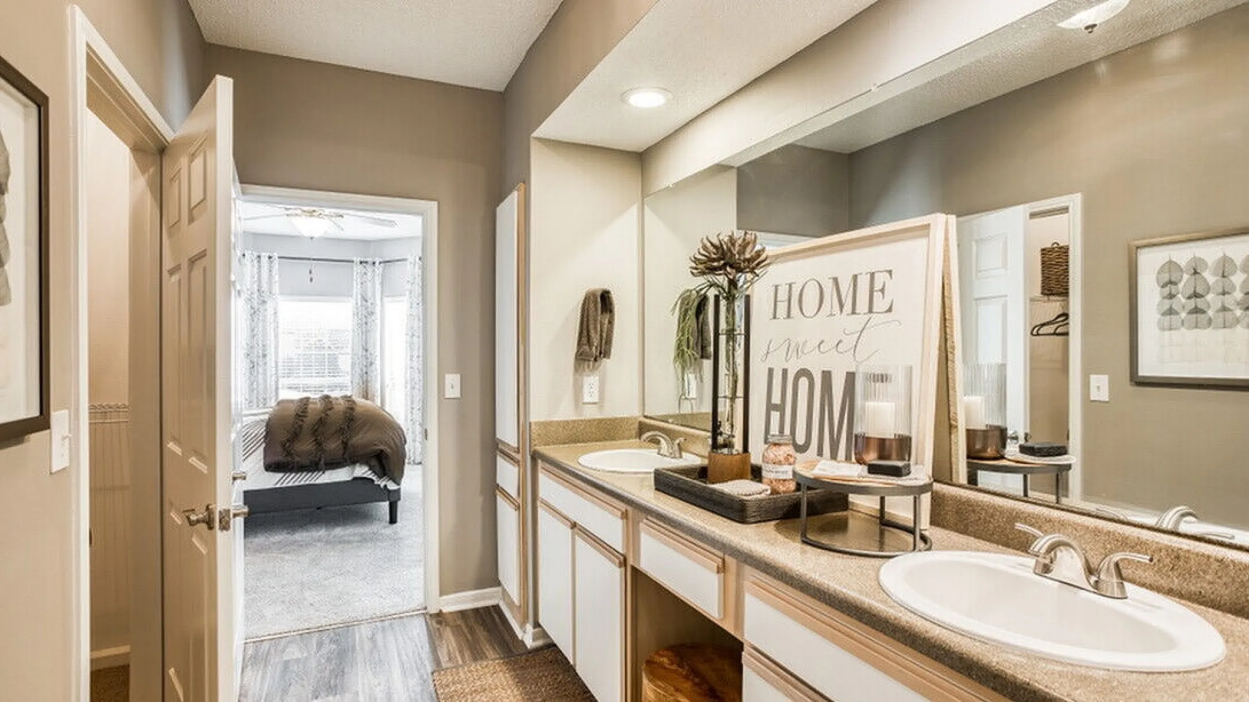 Inviting bathroom with dual sinks, elegant decor, and warm lighting, leading to a cozy bedroom with plush bedding.