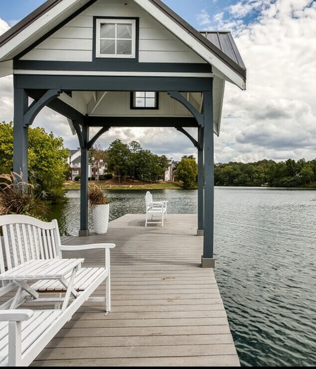Charming lakeside gazebo with serene water views, featuring white benches and lush greenery, perfect for tranquil living.