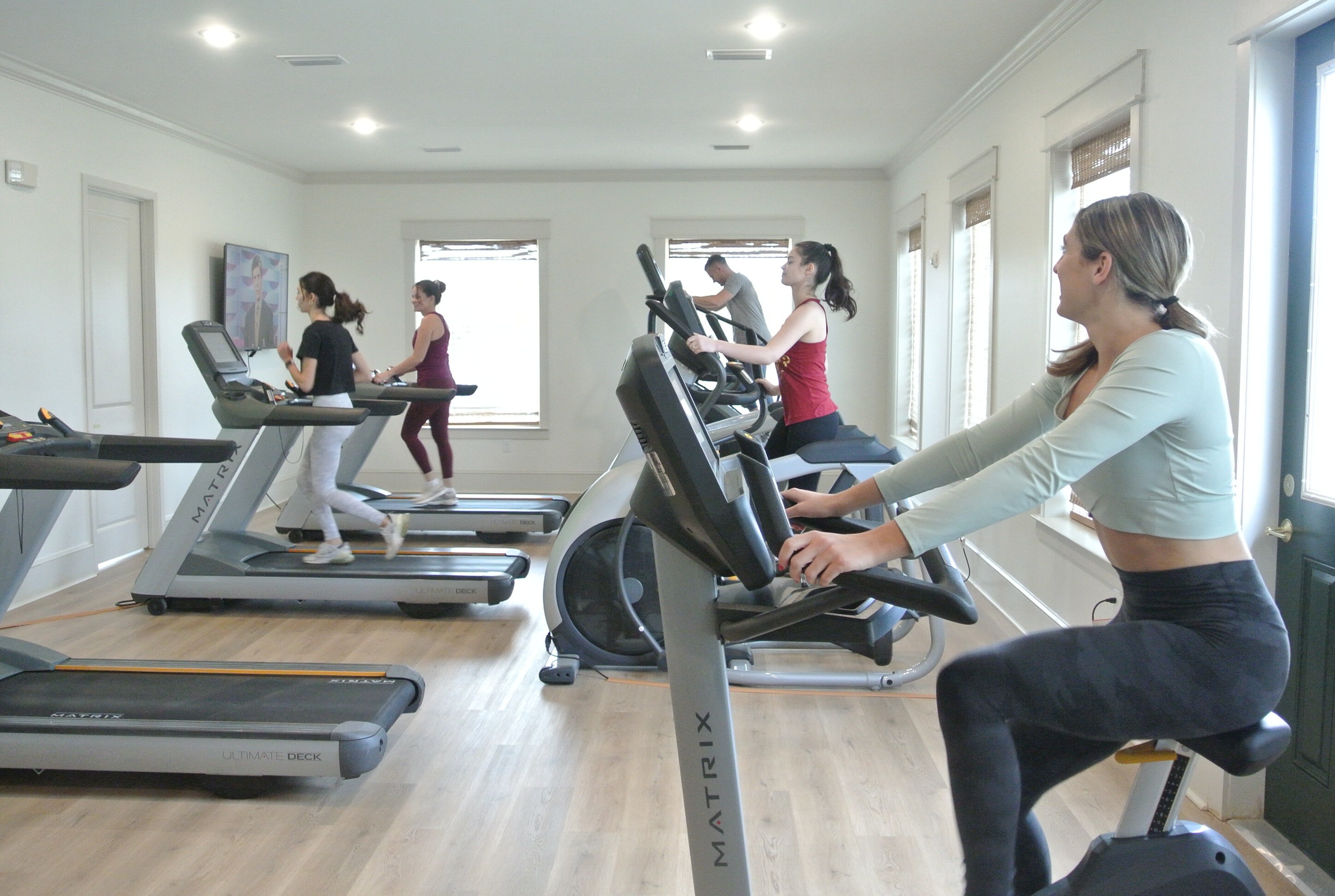 Modern fitness center with vibrant atmosphere featuring people using treadmills and stationary bikes, surrounded by natural light.
