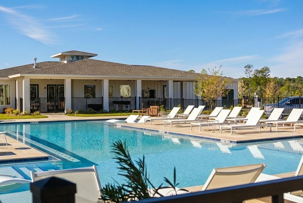 Luxurious apartment community featuring a sparkling outdoor pool, stylish deck chairs, and a modern clubhouse under a clear blue sky.