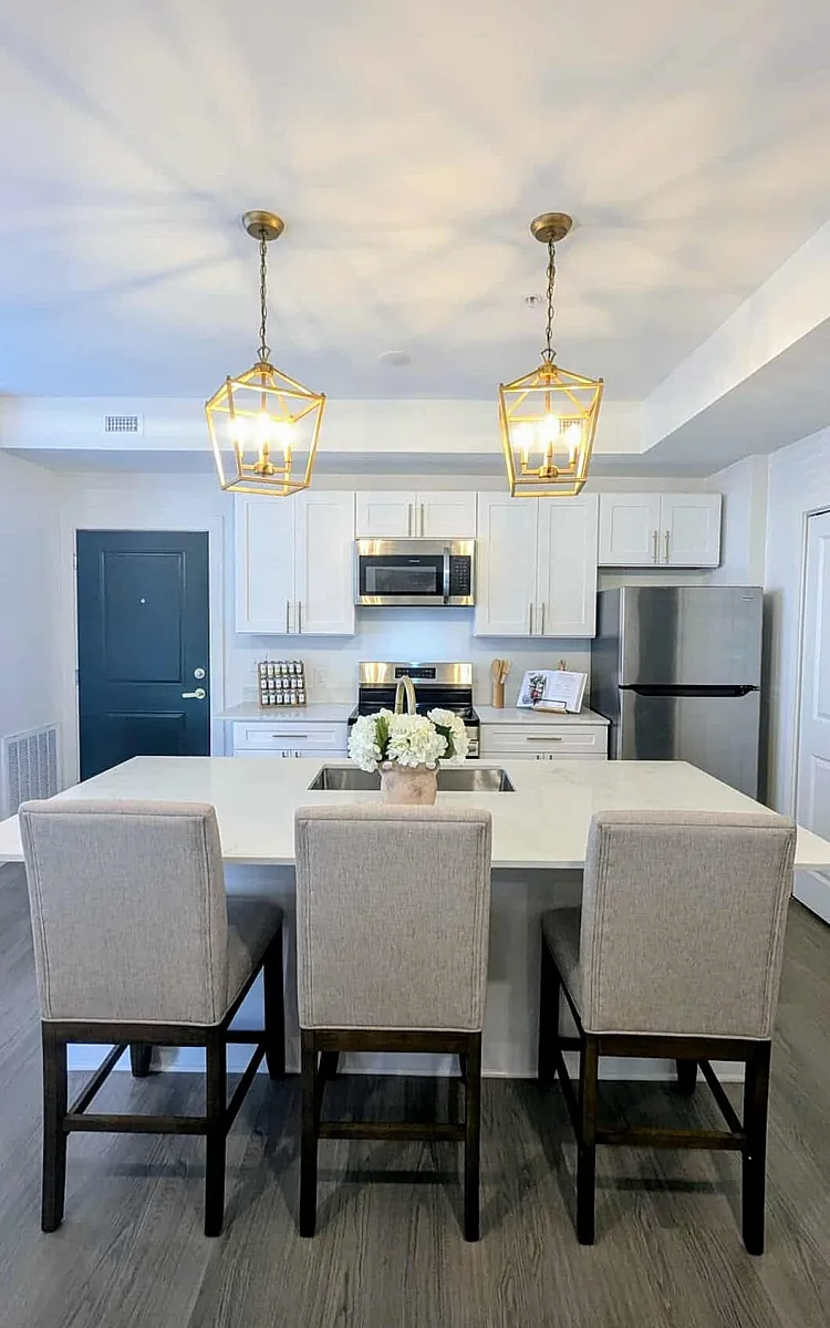 Elegant modern kitchen featuring sleek white cabinets, stainless steel appliances, and a stylish island with chic lighting fixtures.