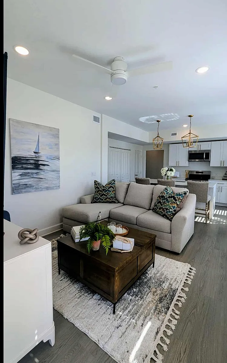 Bright and modern living area with an elegant open-plan design, featuring a cozy sofa, stylish coffee table, and a chic kitchen in the background, enhanced by natural light and decorative accents.