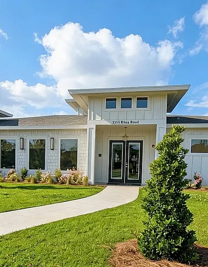 Charming single-story house with modern architecture, surrounded by manicured lawns and lush greenery under a bright blue sky.