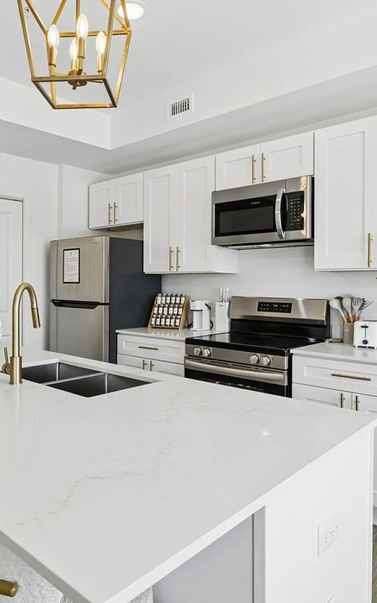 Sleek modern kitchen with white cabinetry, elegant pendant lighting, and a spacious quartz island, perfect for entertaining.