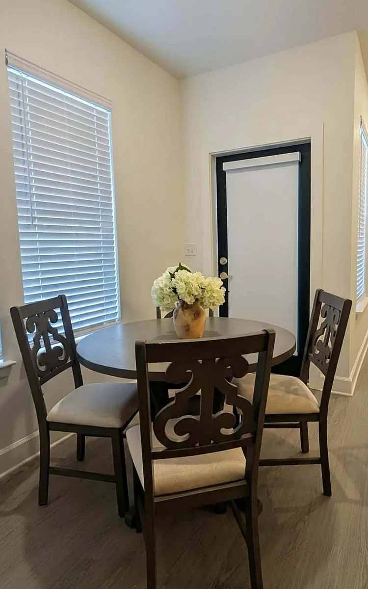Charming dining nook with elegant dark wood table and chairs, featuring a tasteful flower centerpiece and natural light streaming through stylish blinds.