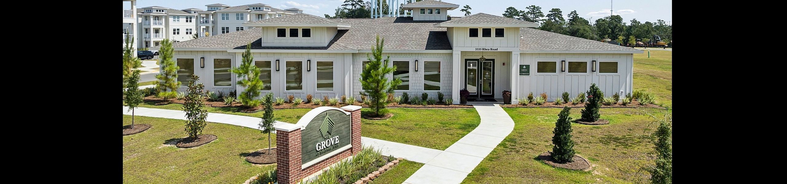 Charming apartment complex with lush landscaping and modern white exterior, accentuated by a prominent water tower.