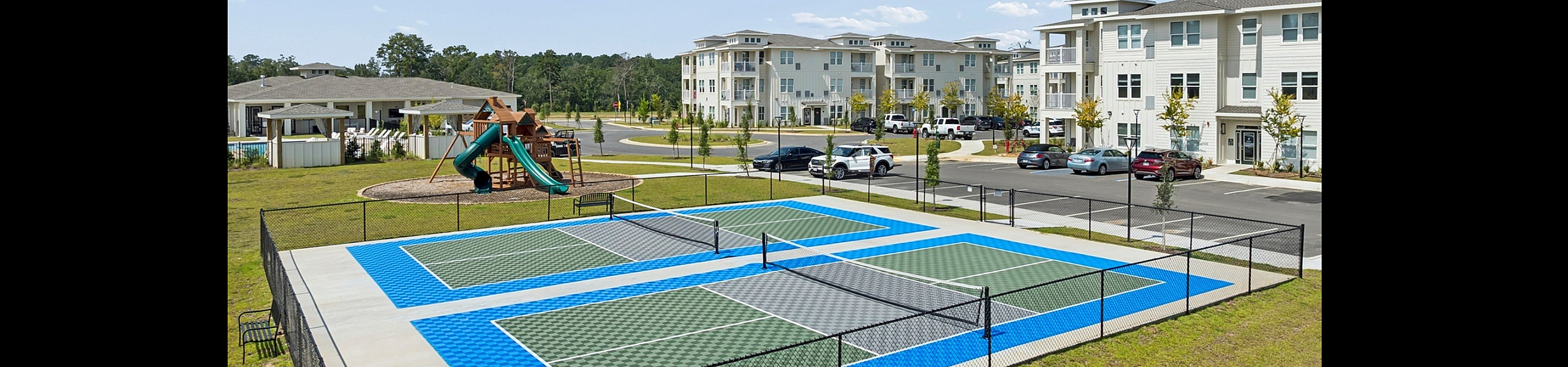 Vibrant apartment community showcasing modern tennis courts and a playground amidst lush greenery and stylish buildings.