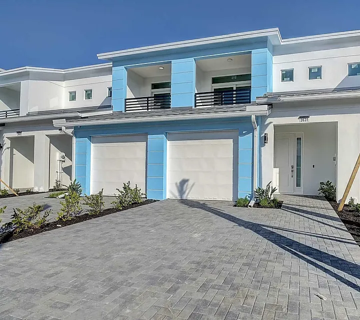Modern townhouse exterior featuring vibrant blue accents, dual garages, and elegant palm trees, exuding coastal charm.