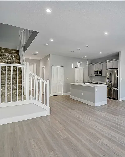 Modern open-concept living space featuring a sleek kitchen with stainless steel appliances, bright hardwood floors, and a stylish staircase.