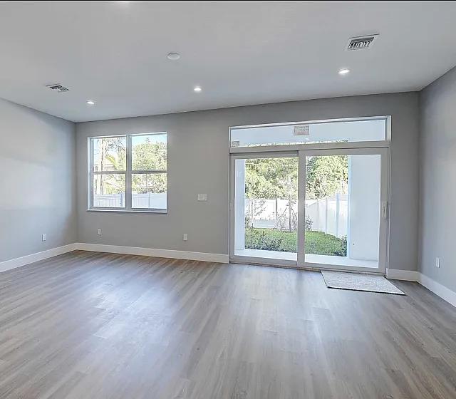 Bright and airy living space with sleek hardwood floors and large windows offering a serene garden view.