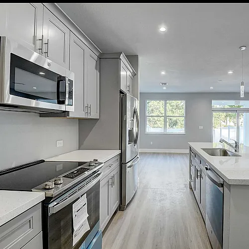 Sleek modern kitchen with stainless steel appliances, elegant pendant lighting, and a spacious open floor plan leading to a bright living area.