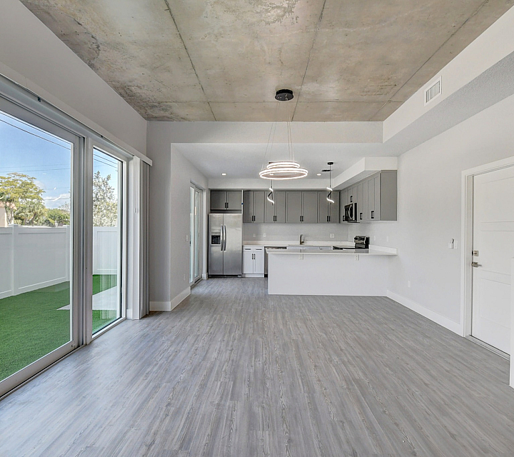 Modern open-concept living space with sleek gray cabinetry, stainless steel appliances, and vibrant natural light from large sliding glass doors.