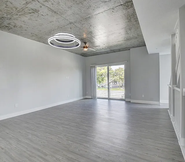 Modern living space with industrial chic design, featuring polished concrete ceiling, elegant ring chandelier, and expansive sliding glass doors leading to a balcony with a scenic view.