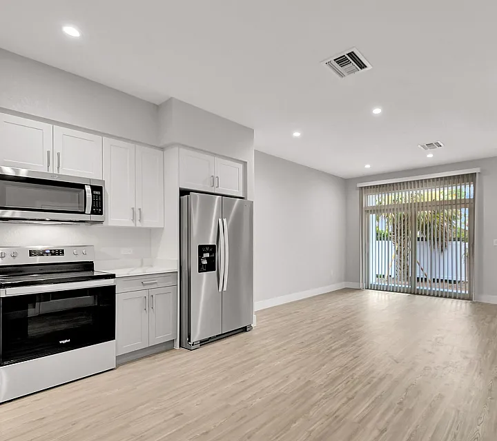 Modern open-plan kitchen with stainless steel appliances, sleek cabinets, and large living area with natural light and patio view.