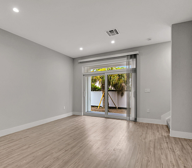 Modern living room with sleek wooden flooring, large sliding glass doors leading to a lush garden view, and abundant natural light.