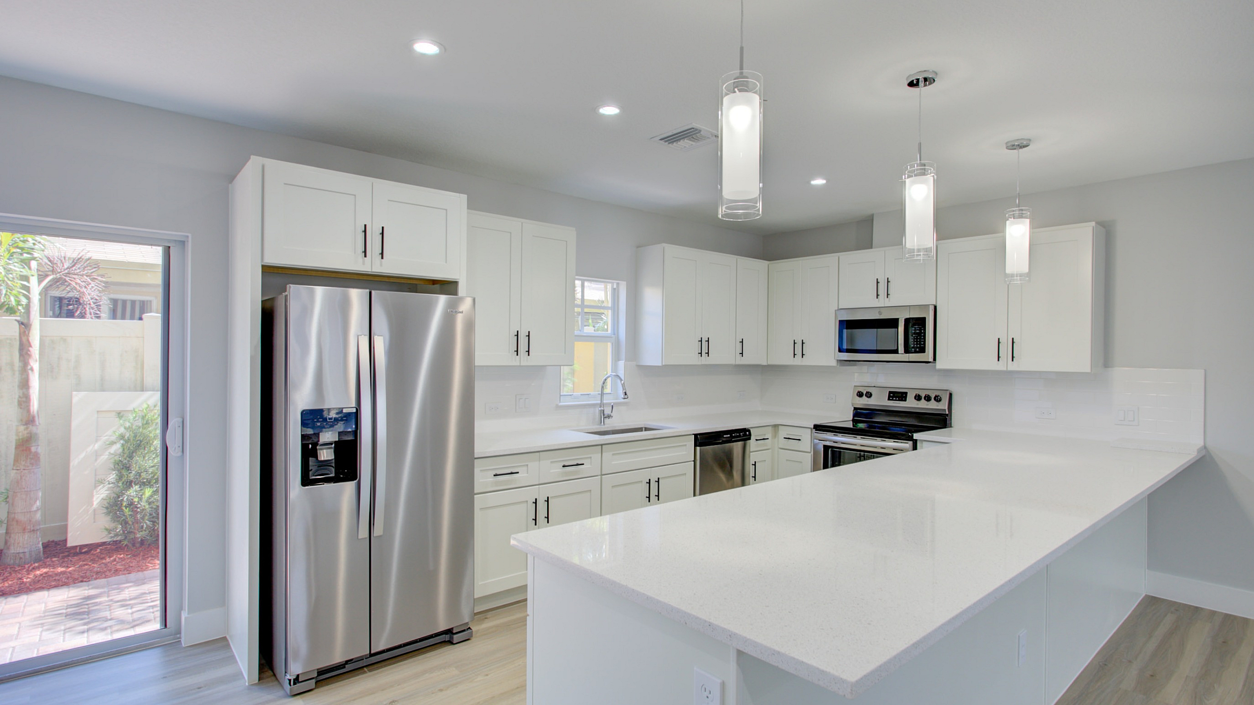 Modern kitchen with sleek stainless steel appliances, elegant white cabinetry, and a spacious quartz countertop island under stylish pendant lighting.