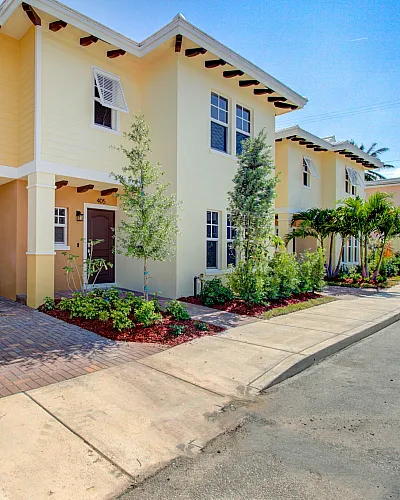 Charming townhomes with vibrant yellow exteriors, lush landscaping, and spacious driveways in a serene neighborhood.