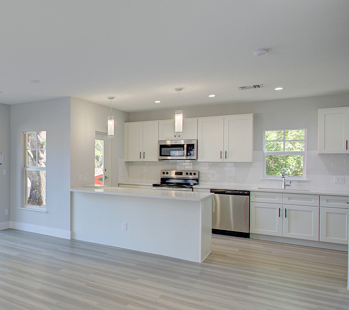 Modern open-concept living space with bright natural light, featuring sleek white cabinetry, stainless steel appliances, and elegant wood flooring.