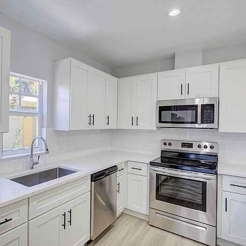 Modern kitchen with pristine white cabinetry, sleek countertops, stainless steel appliances, and ample natural light.