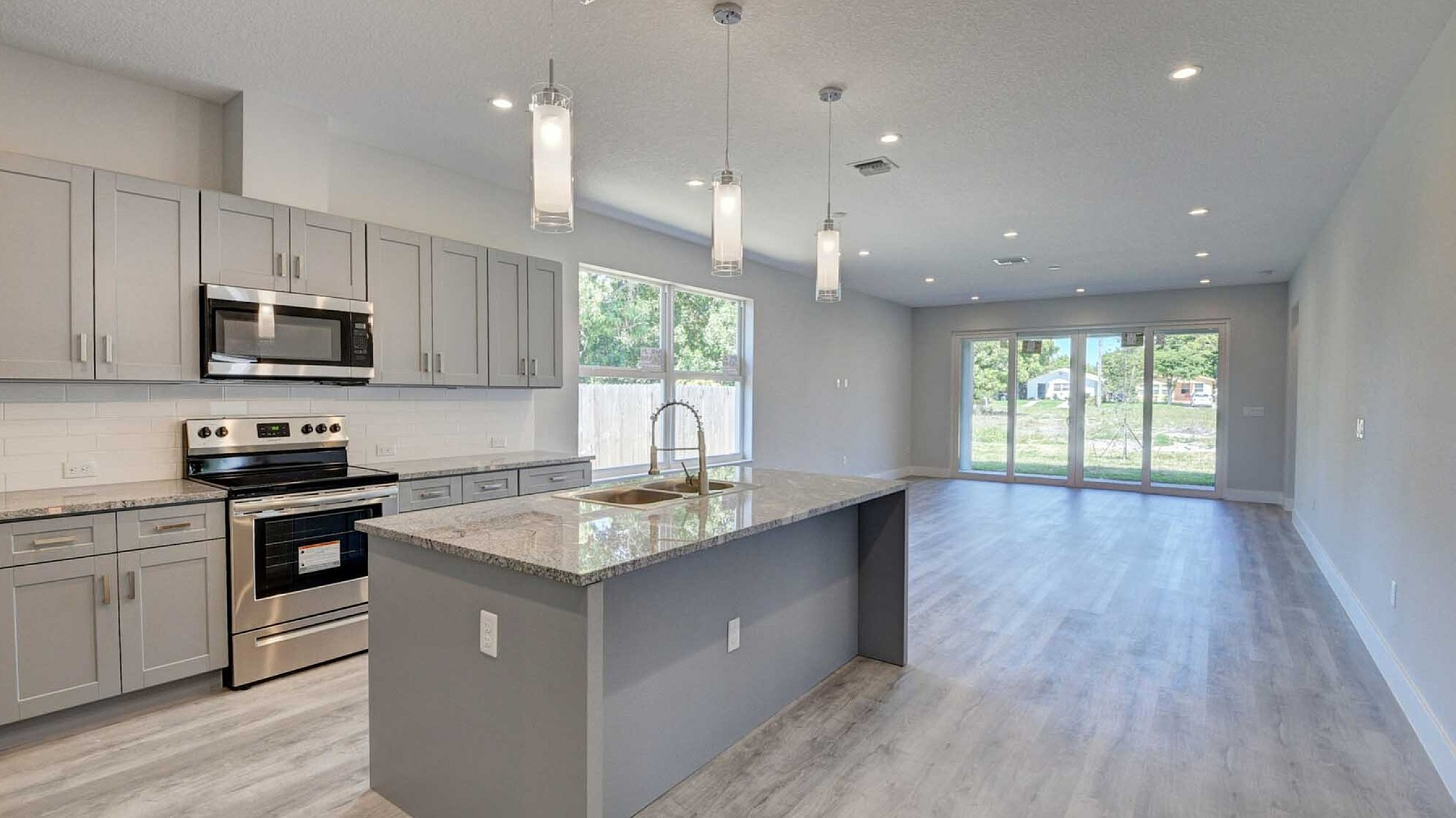 Modern open-concept kitchen and living area with sleek gray cabinets, granite countertops, and large windows inviting ample natural light.
