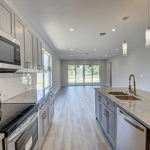 Contemporary open-plan kitchen with elegant granite countertops, modern stainless steel appliances, and bright natural light from large windows overlooking greenery.