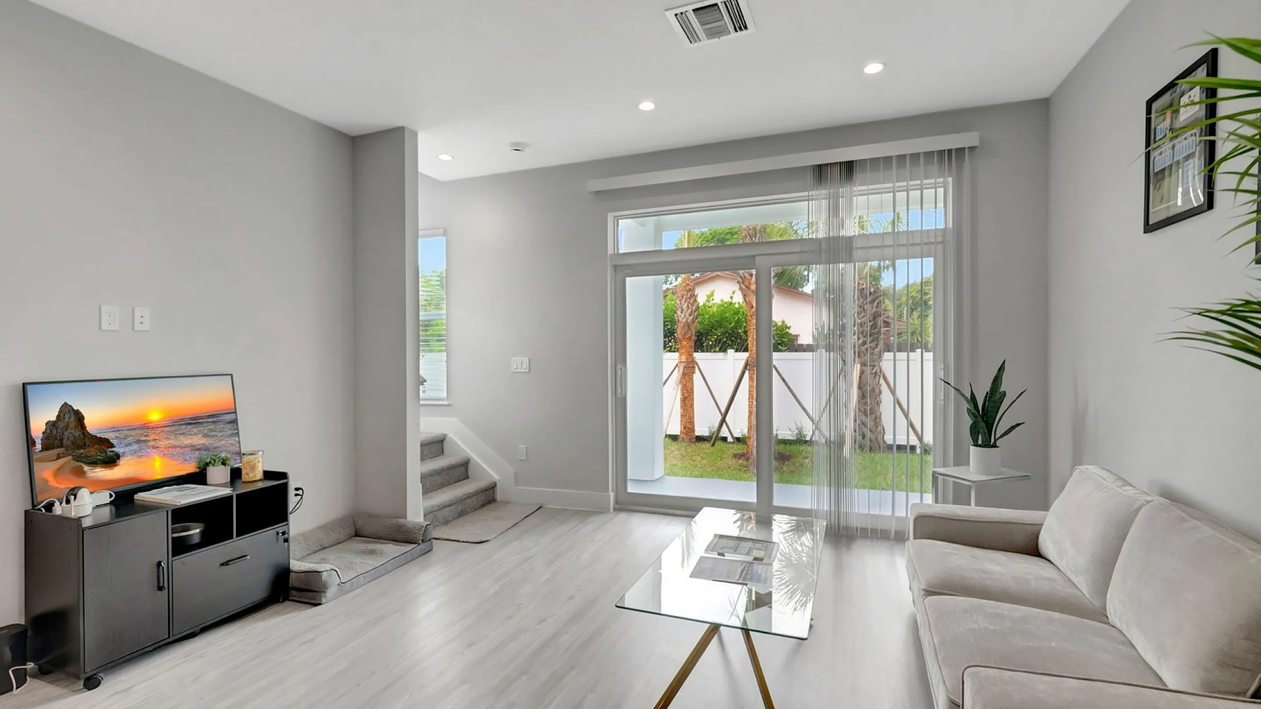 Bright and modern living room with elegant glass coffee table, cozy sofa, and large sliding doors opening to a lush garden view.