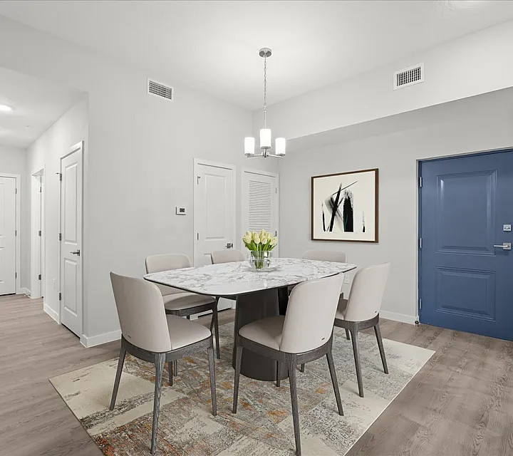 Chic dining area with a marble table, modern chairs, and elegant lighting, enhanced by stylish artwork and a vibrant blue door.