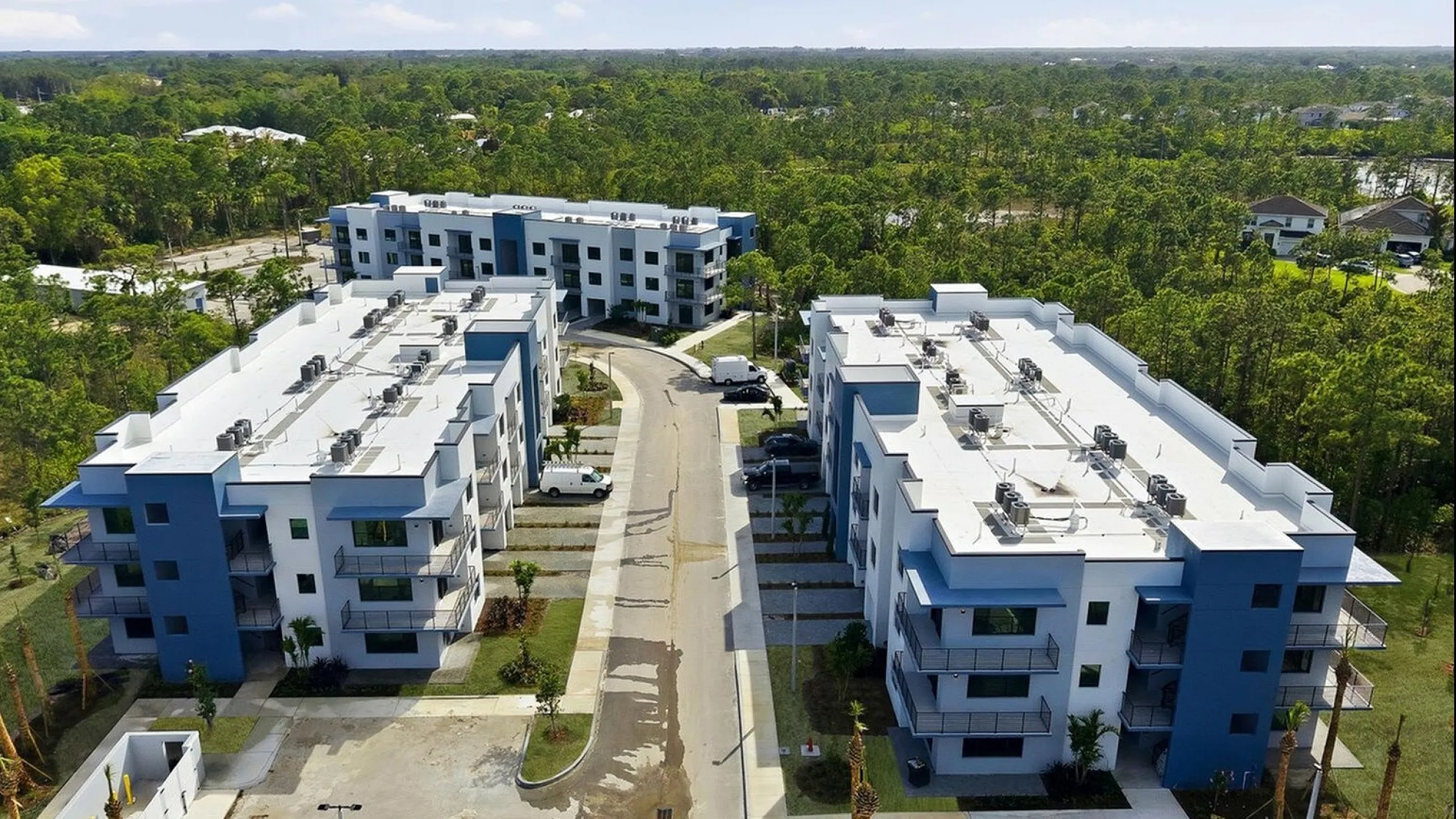 Aerial view of modern blue and white apartment complexes surrounded by greenery, featuring spacious balconies and neatly maintained grounds for a serene living environment.