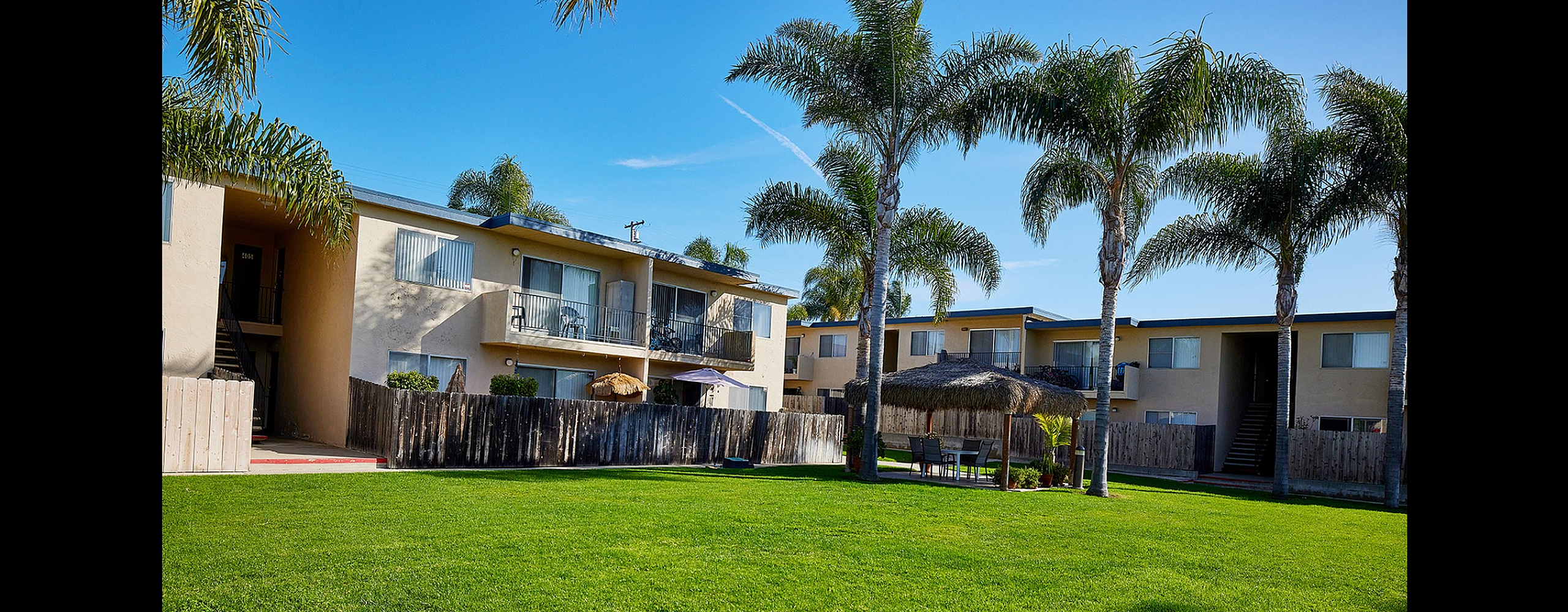 Inviting apartment complex with lush green lawns, palm trees, and cozy outdoor seating, perfect for relaxation and community gatherings.