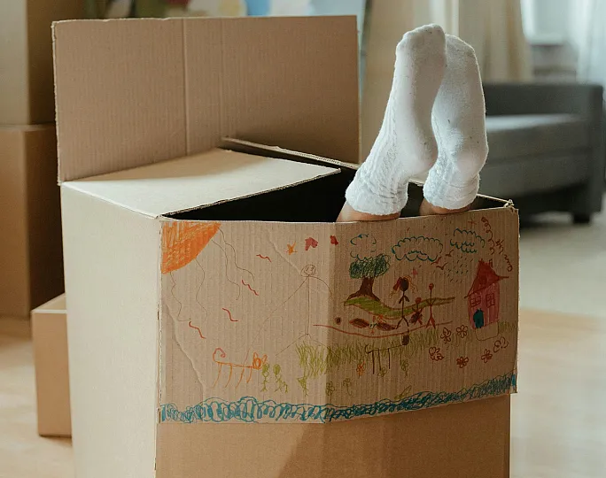 Charming apartment scene with a playful touch, featuring a decorated moving box with a child's feet in cozy socks peeking out, adding warmth and creativity to the modern living space.